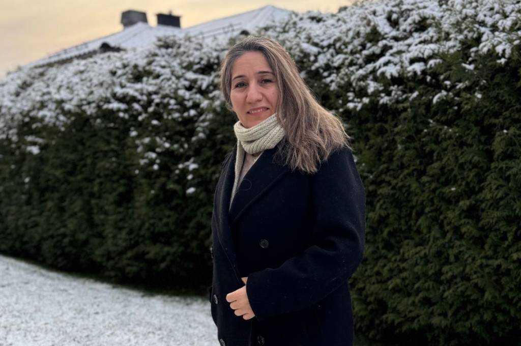 Nask står ute foran en grønn hekk som er snødekket på toppen!''