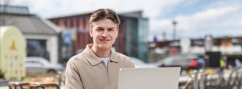Mannlig student på Fagskolen Diakonova sitter og jobber laptop på utekafe