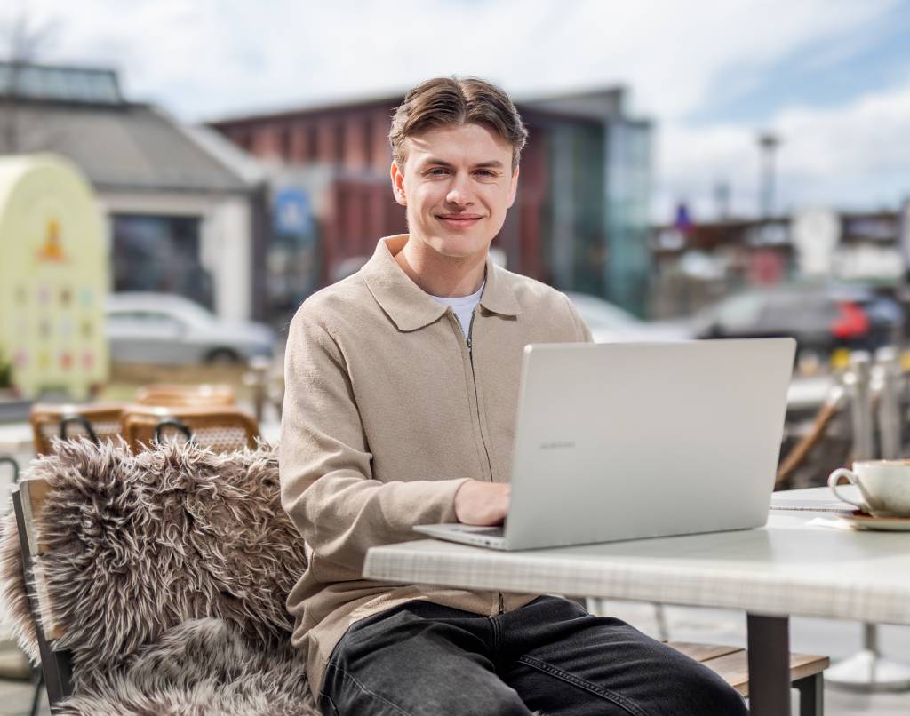 Mannlig student på Fagskolen Diakonova sitter og jobber laptop på utekafe