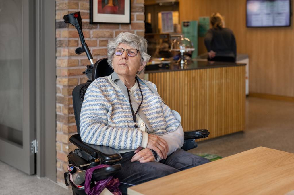 Eldre dame sitter i rullestoll med arm i fatle og ser tankefull utover!''
