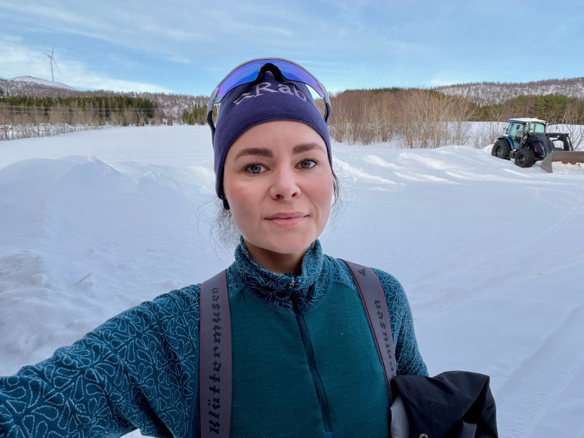 Sara står ute en vinterdag med skog og en traktor i bakgrunnen