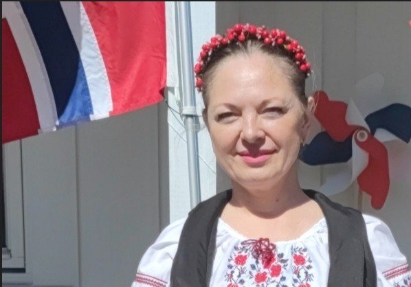 Olga Labazova ser i kamerat og smiler med et norsk flagg i bakgrunnen
