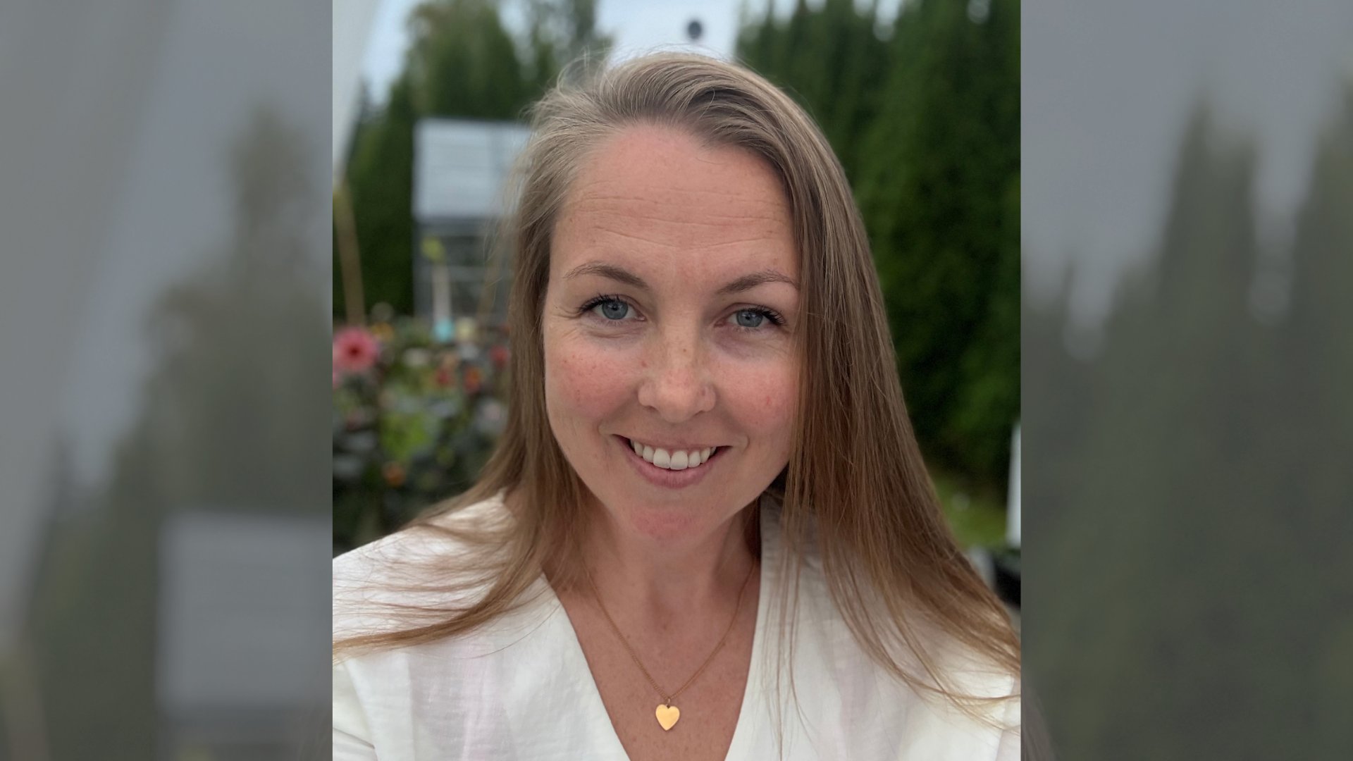 Kristin smiler til kamera foran en grønn hage med blomster i bakgrunnen