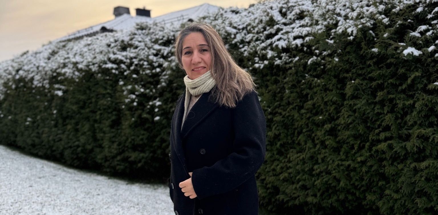 Nask står ute foran en grønn hekk som er snødekket på toppen