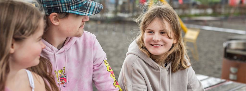 Tre barn sitter på en benk og snakker sammen