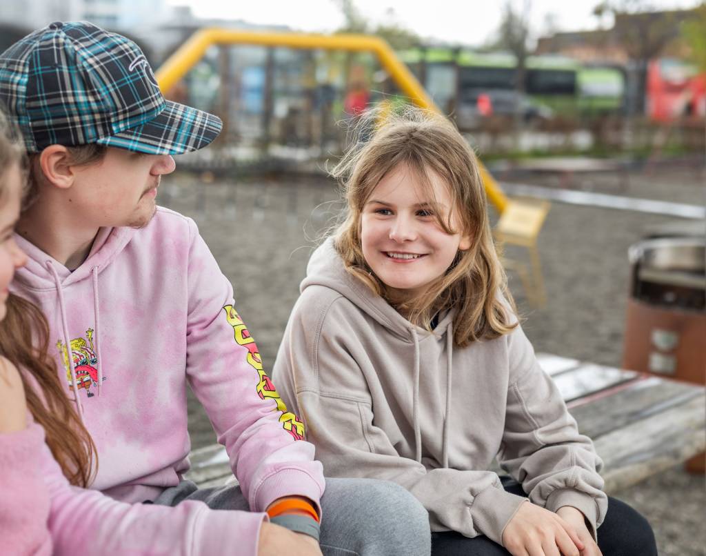 Tre barn sitter på en benk og snakker sammen