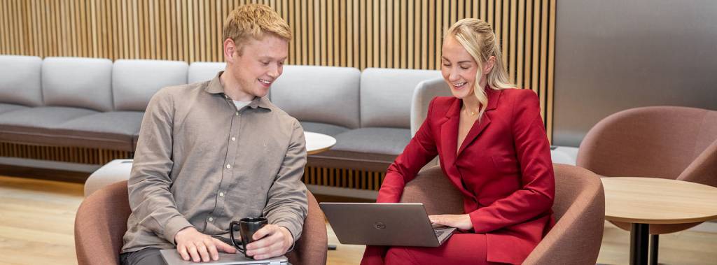 To unge voksne, en mann og en kvinne, som smilende ser på en bærbar PC sammen.