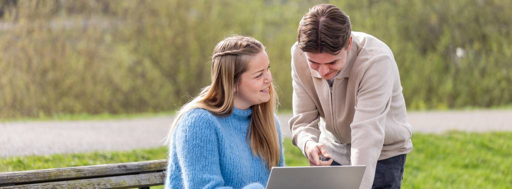 Studenter ved Fagskolen Diakonova, en jente som sitter på en benk og gutt som lener seg over og diskuterer mens de ser på laptop