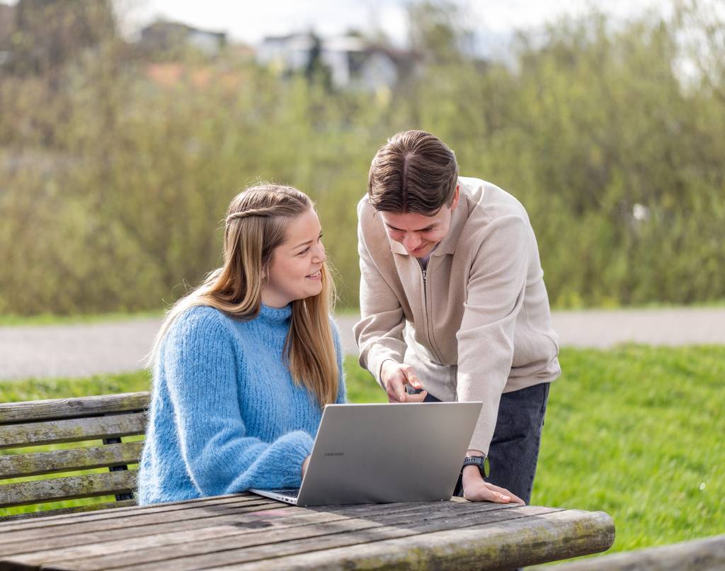 Studenter ved Fagskolen Diakonova, en jente som sitter på en benk og gutt som lener seg over og diskuterer mens de ser på laptop