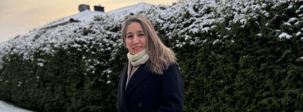 Nask står ute foran en grønn hekk som er snødekket på toppen