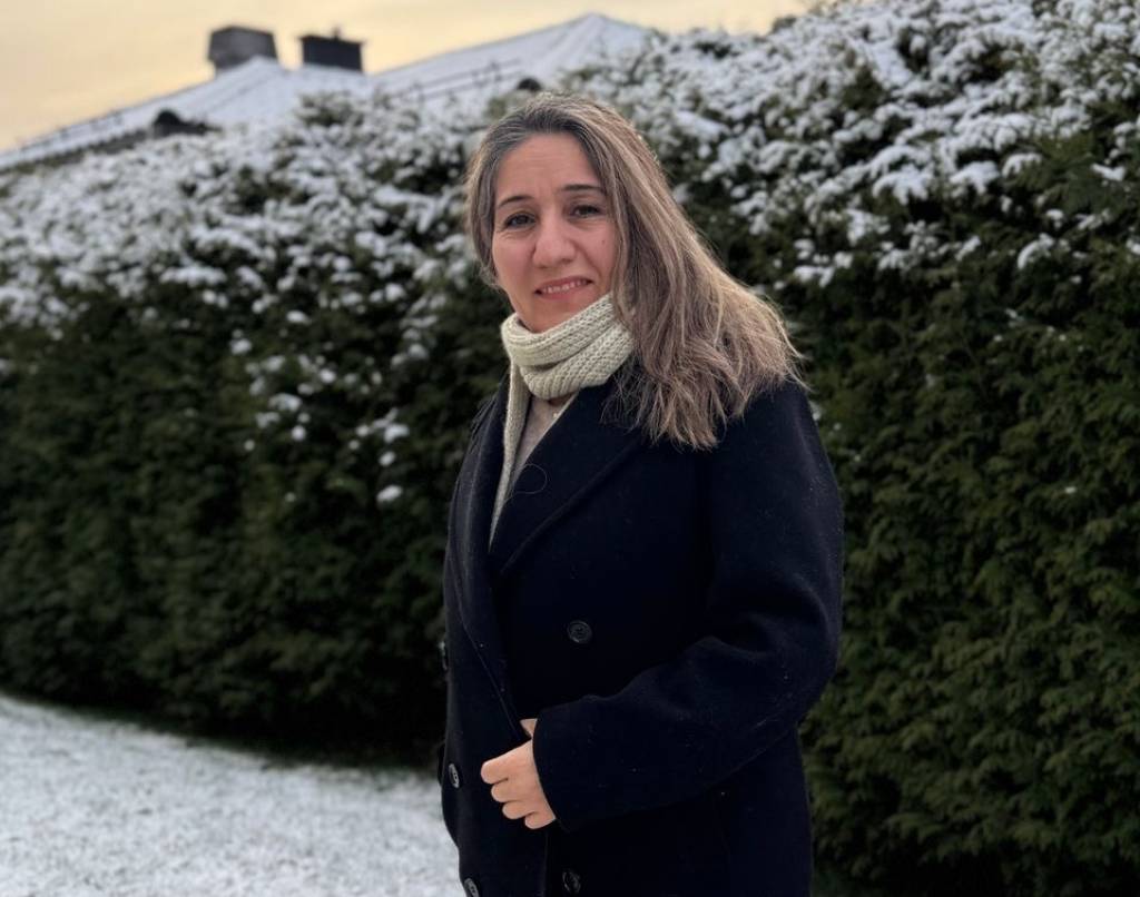 Nask står ute foran en grønn hekk som er snødekket på toppen