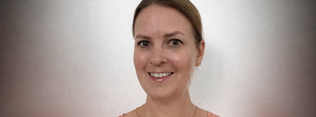 Trine står foran en hvit vegg og smiler