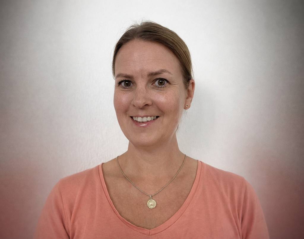 Trine står foran en hvit vegg og smiler