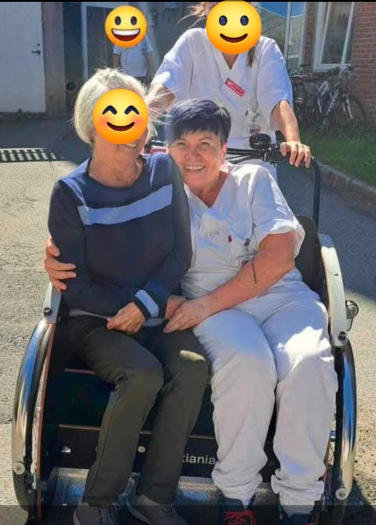 Ljilja på jobb sammen med kolleger og en person hun jobber med. Ansiktene til de andre er dekket av et smileyfjes