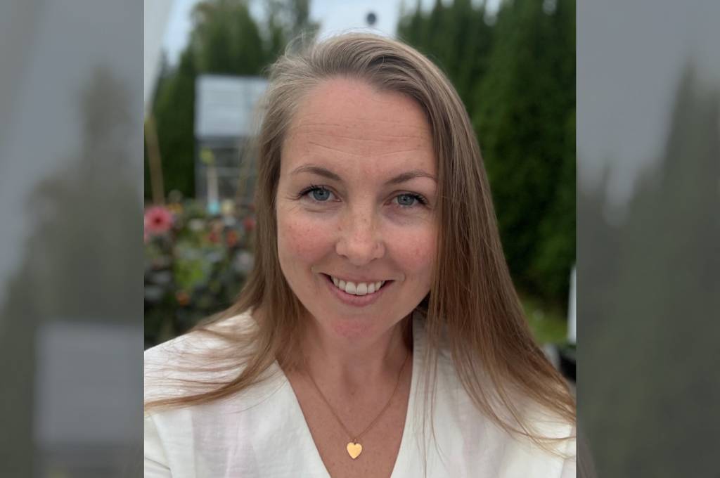 Kristin smiler til kamera foran en grønn hage med blomster i bakgrunnen!''