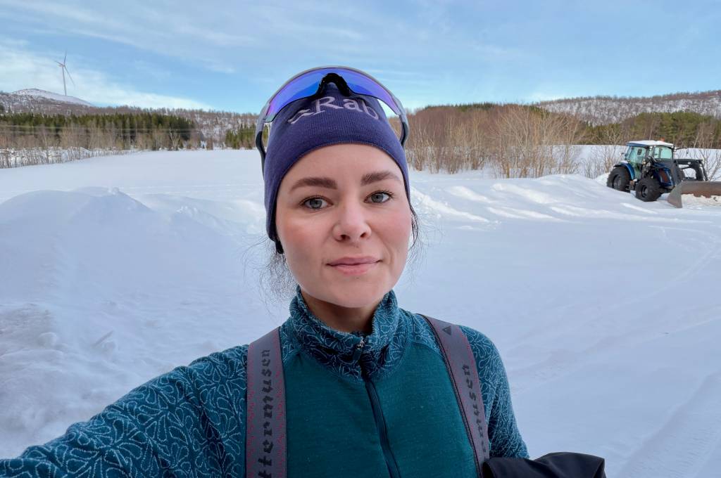 Sara står ute en vinterdag med skog og en traktor i bakgrunnen!''