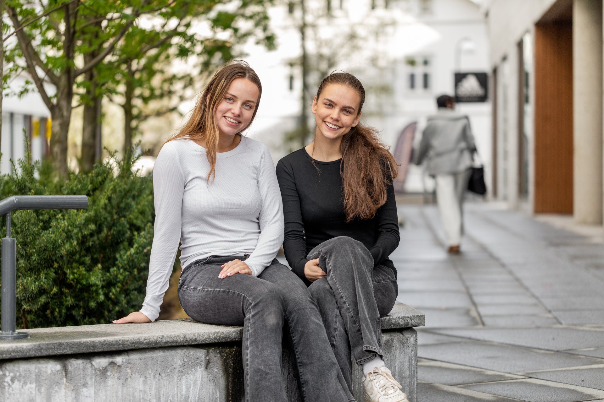 To studenter sitter på en benk og smiler og ser mot kamera