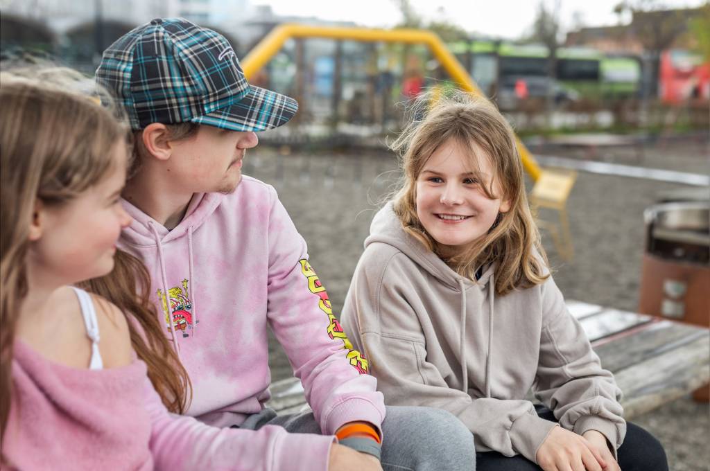 Tre barn sitter på en benk og snakker sammen!''