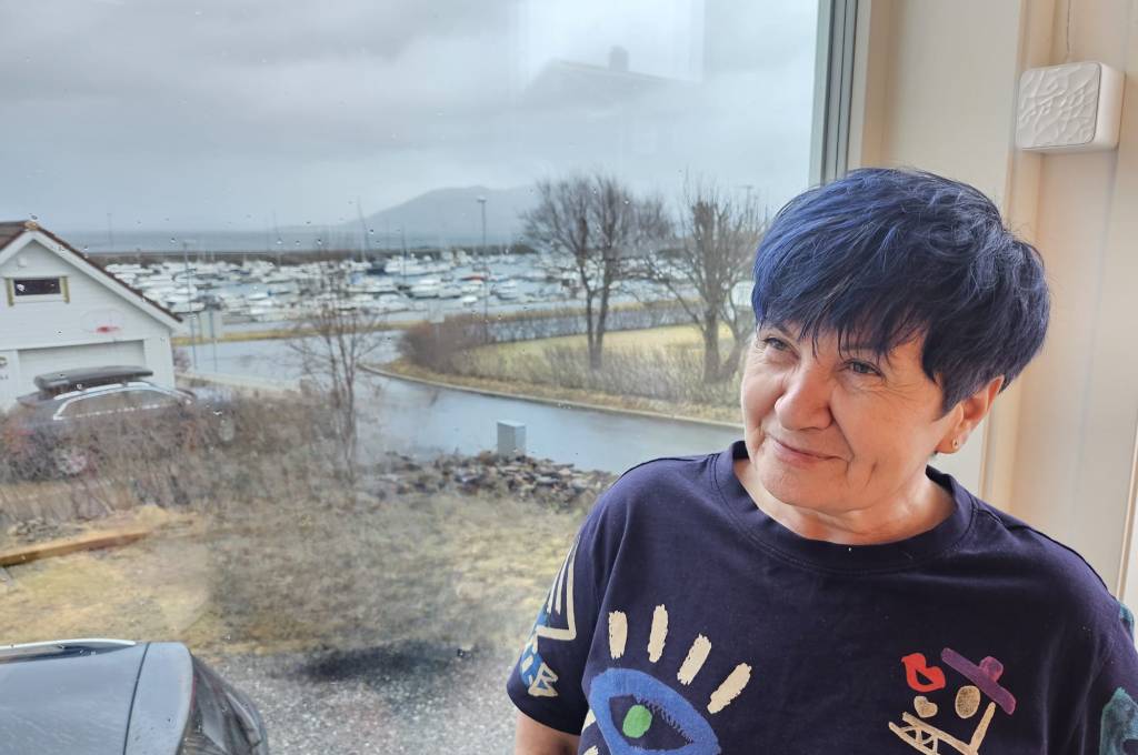 Ljilja sitter foran et vindu med en båthavn i bakgrunnen!''