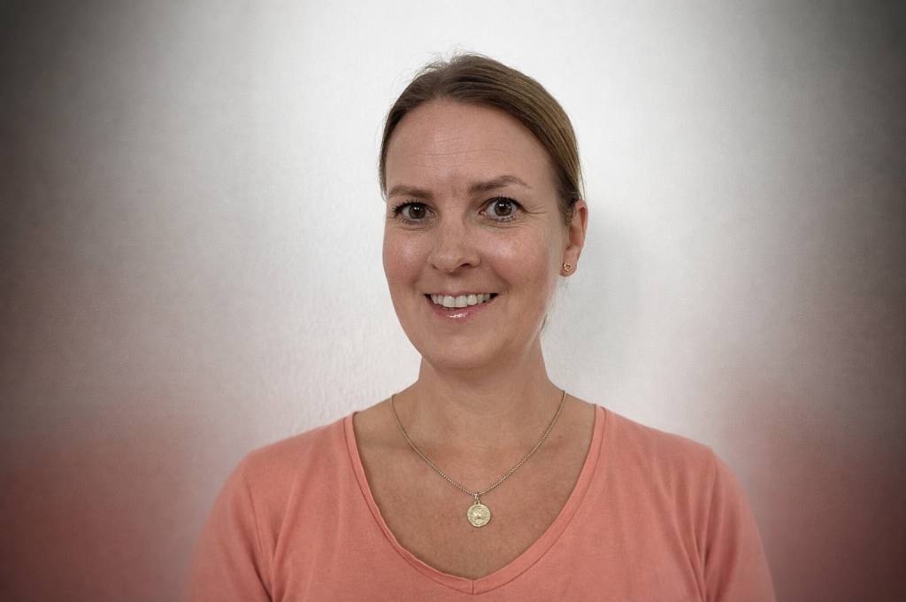 Trine står foran en hvit vegg og smiler!''