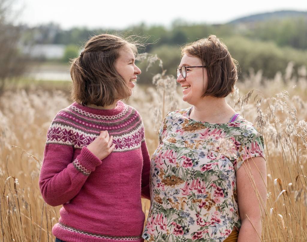 Mor og datter står ute i solen og ser på hverandre imens de smiler